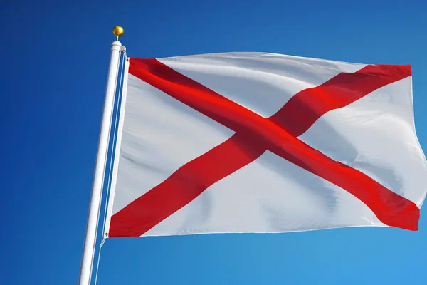 State flag of Alabama, a red Saint Andrew's cross on a white field, flying against a blue sky.