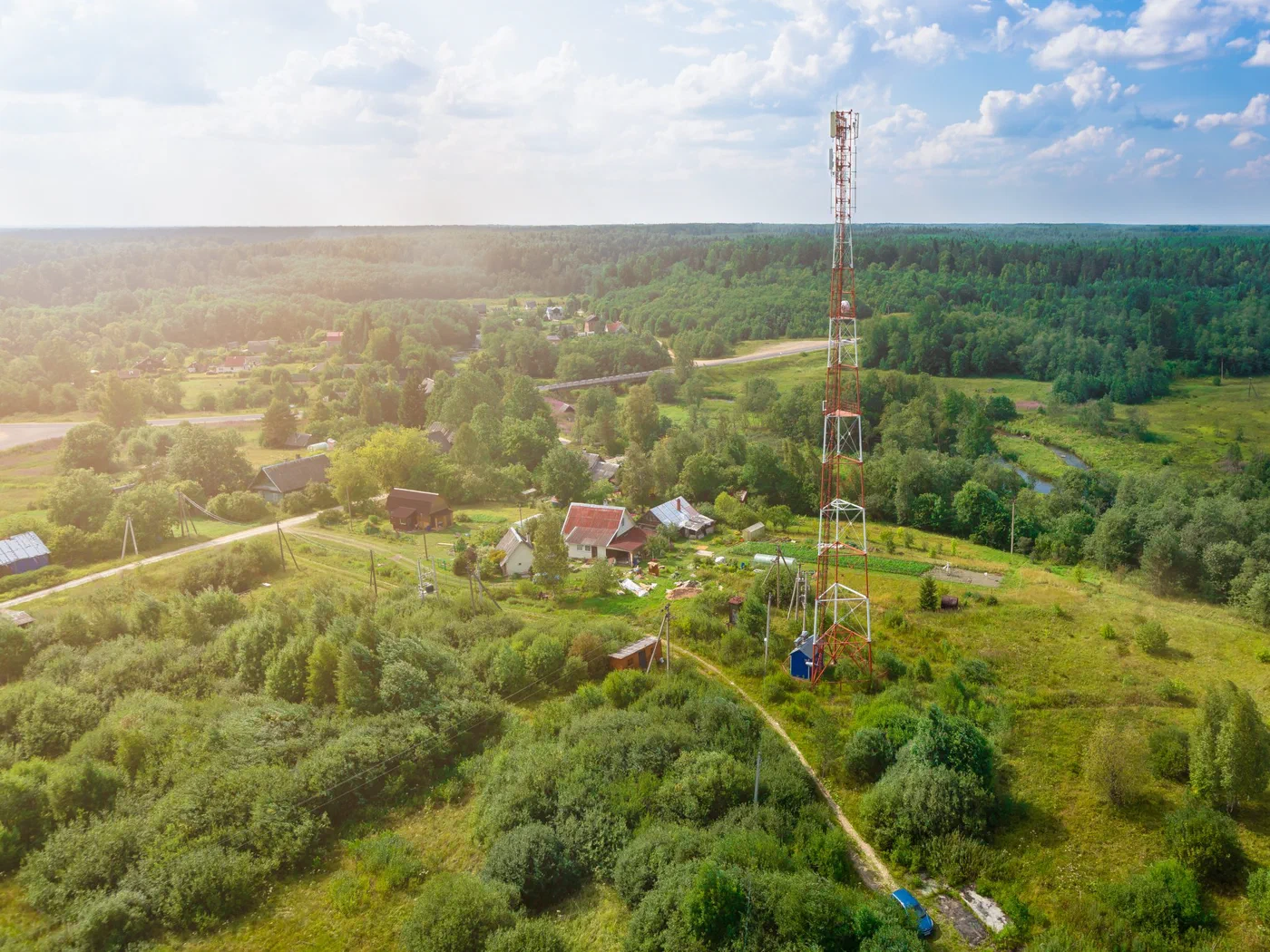 Aerial view of a tall communications tower standing in open rural farmland surrounded by pine forest.
