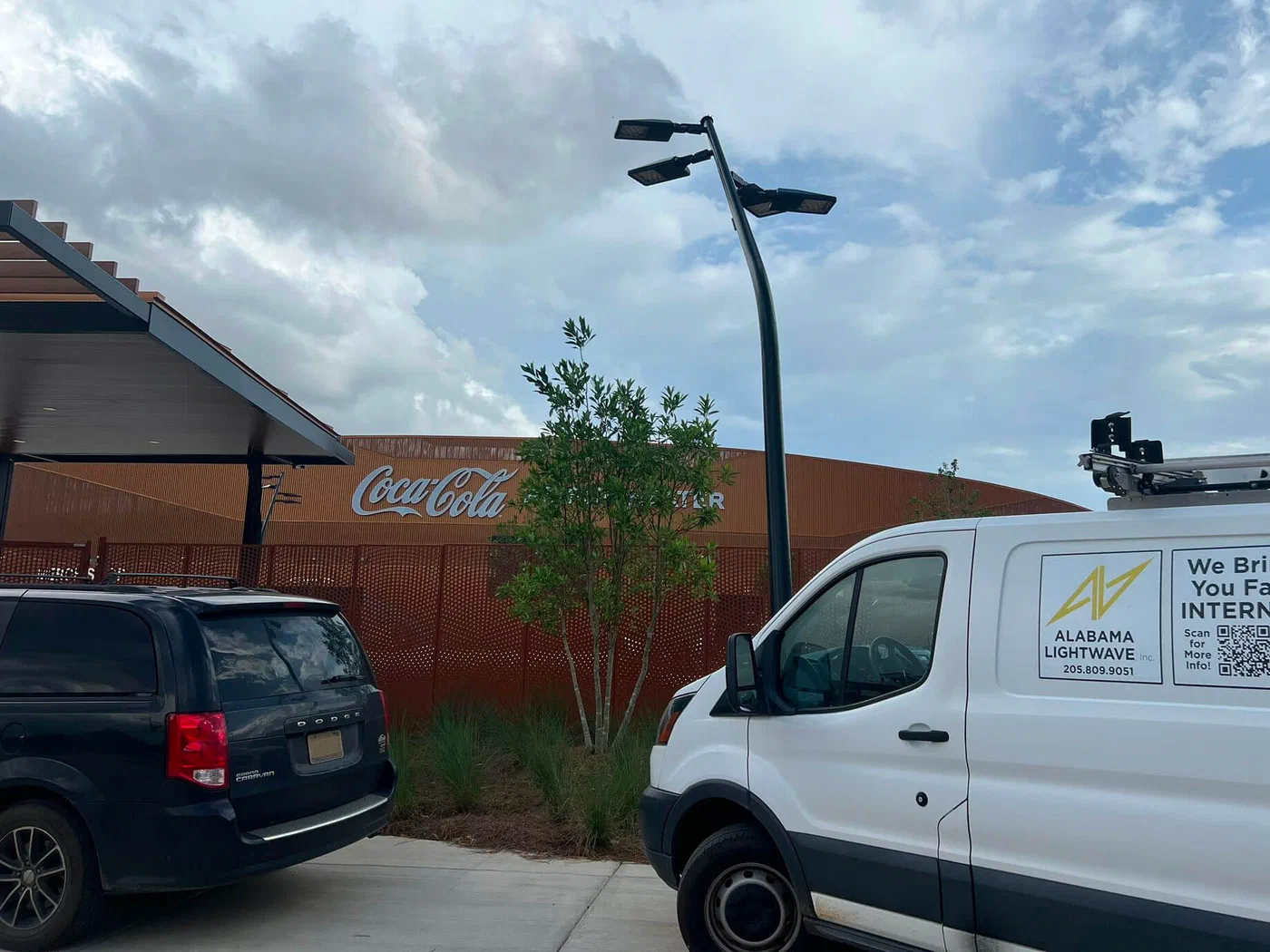 An Alabama Lightwave service van parked outside Birmingham's Coca-Cola Amphitheater, with the venue's perforated copper facade and Coca-Cola signage in the background.